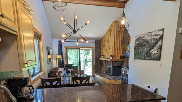 Eine moderne Küche mit Granit Arbeitsplatten, Holzschränken und einer zentralen Kochinsel. Es gibt einen Essbereich mit Tisch und Stühlen sowie einen Kamin.