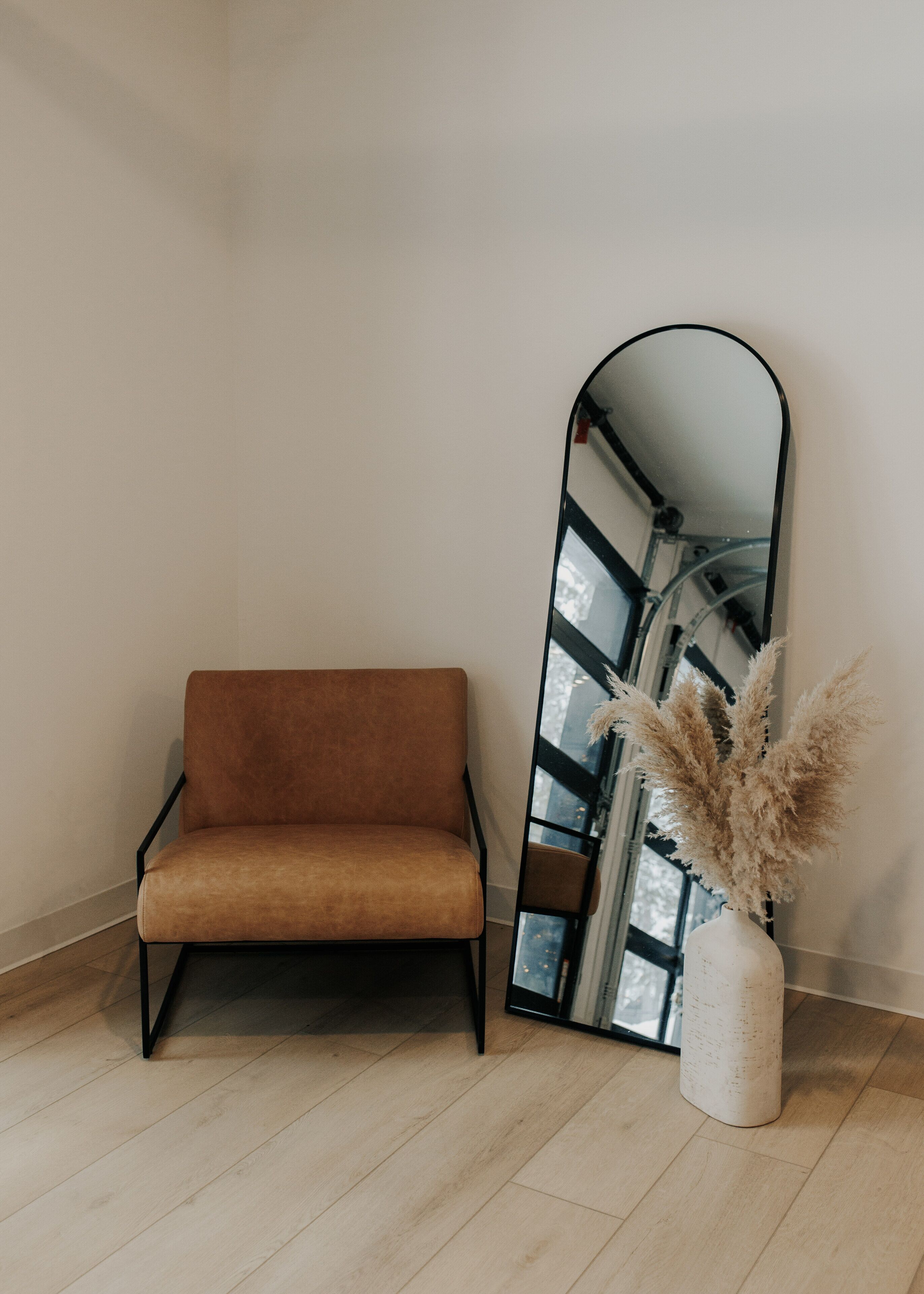 Una habitación con un sofá marrón, un espejo alto y un jarrón con plumas de pluma.