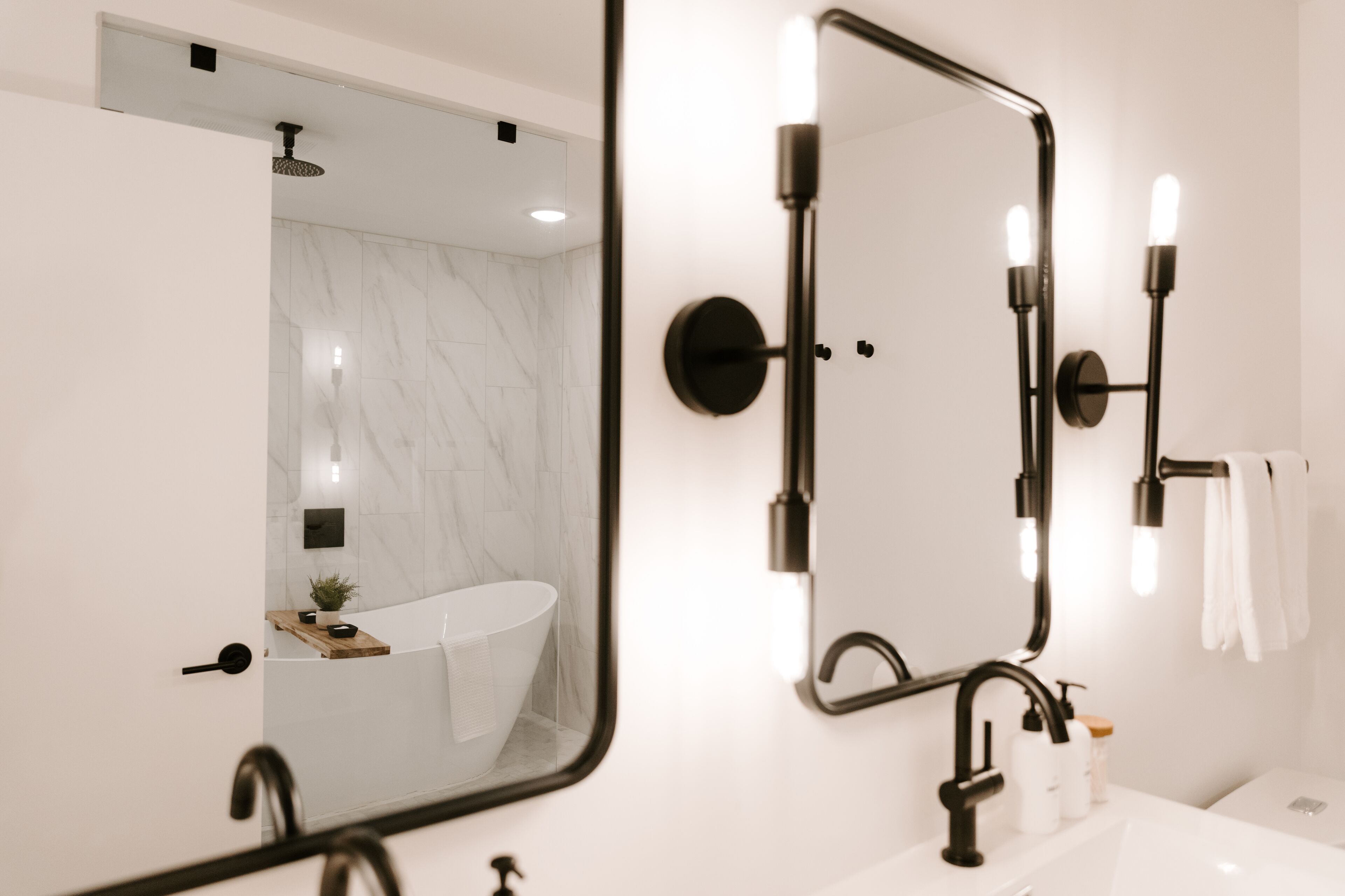 A modern bathroom with a large mirror, a bathtub, and a sink.