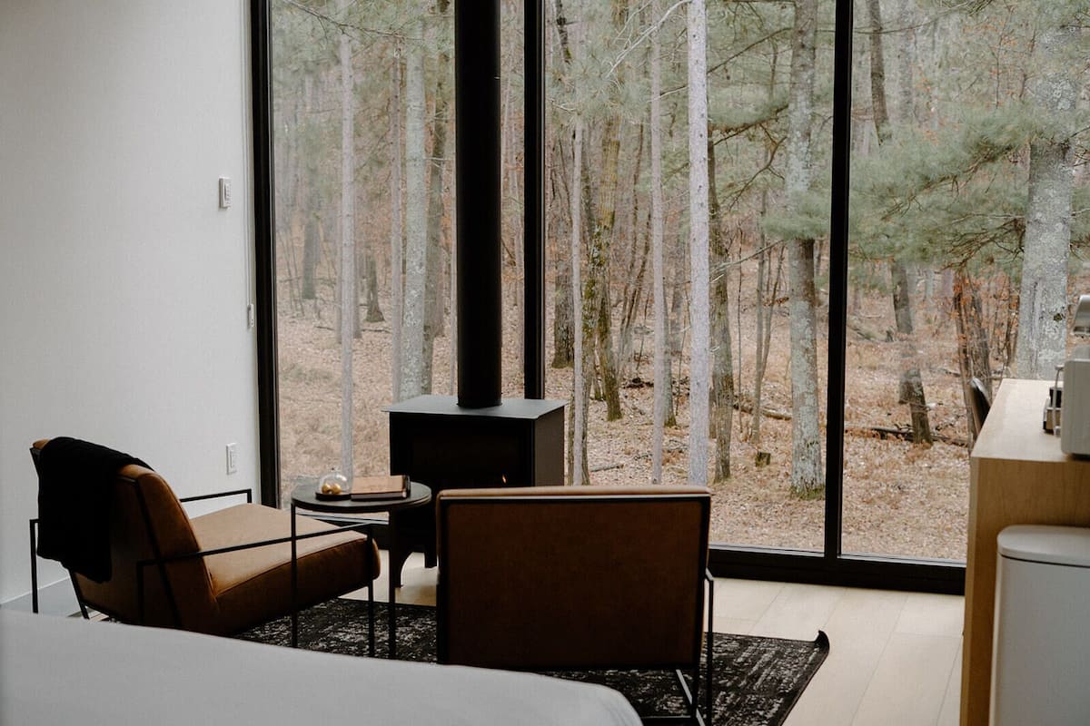 A modern bedroom with a large window, a fireplace, a bed, and a seating area.