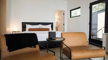 A modern hotel room with a bed, two armchairs, a small table, and a door leading to a balcony.