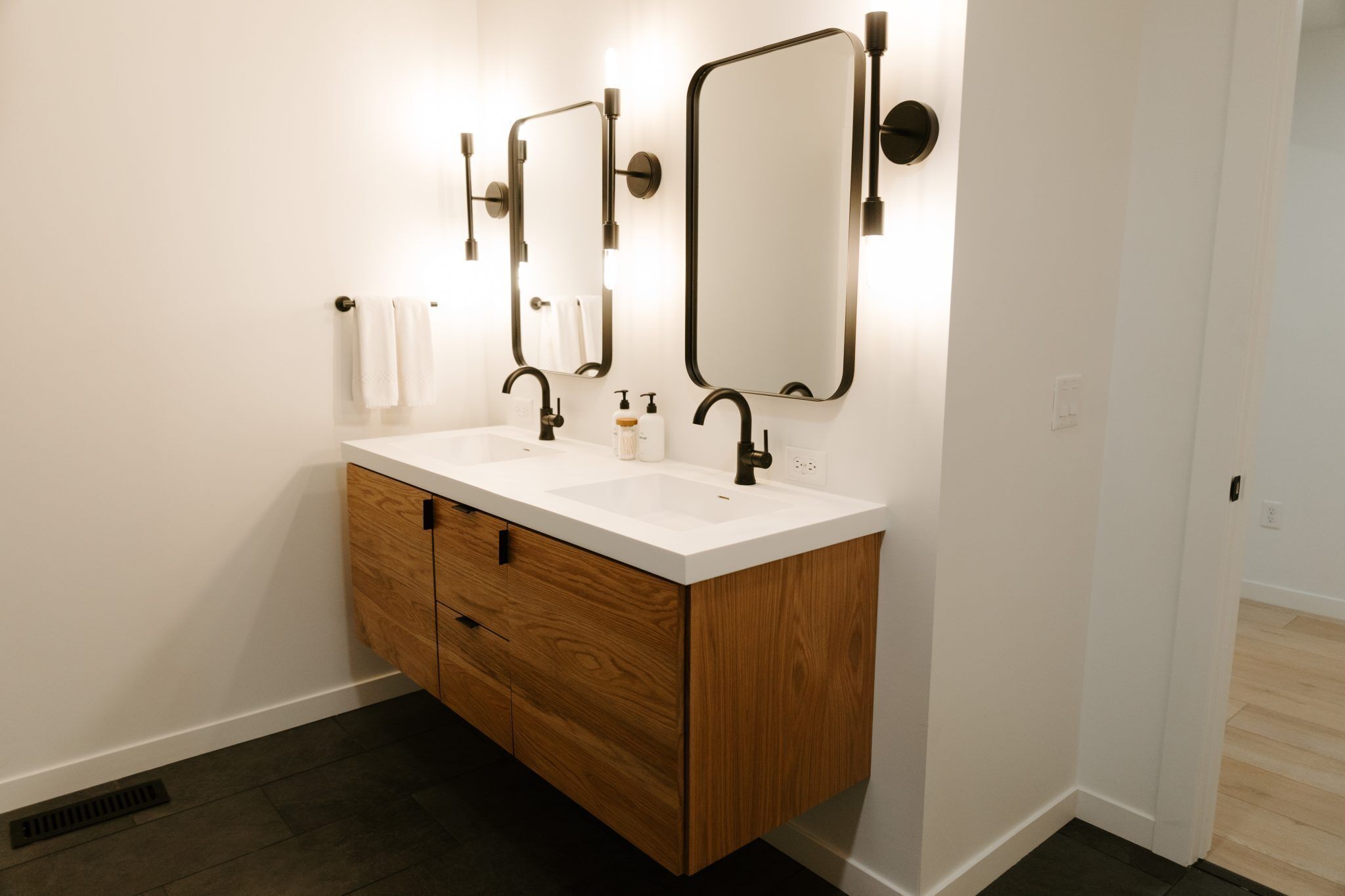 Une salle de bain moderne avec un meuble-lavabo blanc, deux miroirs et un meuble en bois.