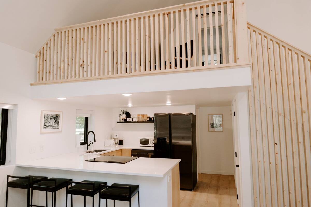 A modern kitchen with a central island, a black refrigerator, and a wooden railing overlooking the space.