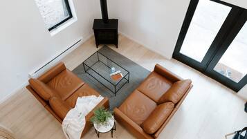 A modern living room with a brown leather sofa, a glass coffee table, and a small side table with a plant. A black fireplace is visible in the corner.