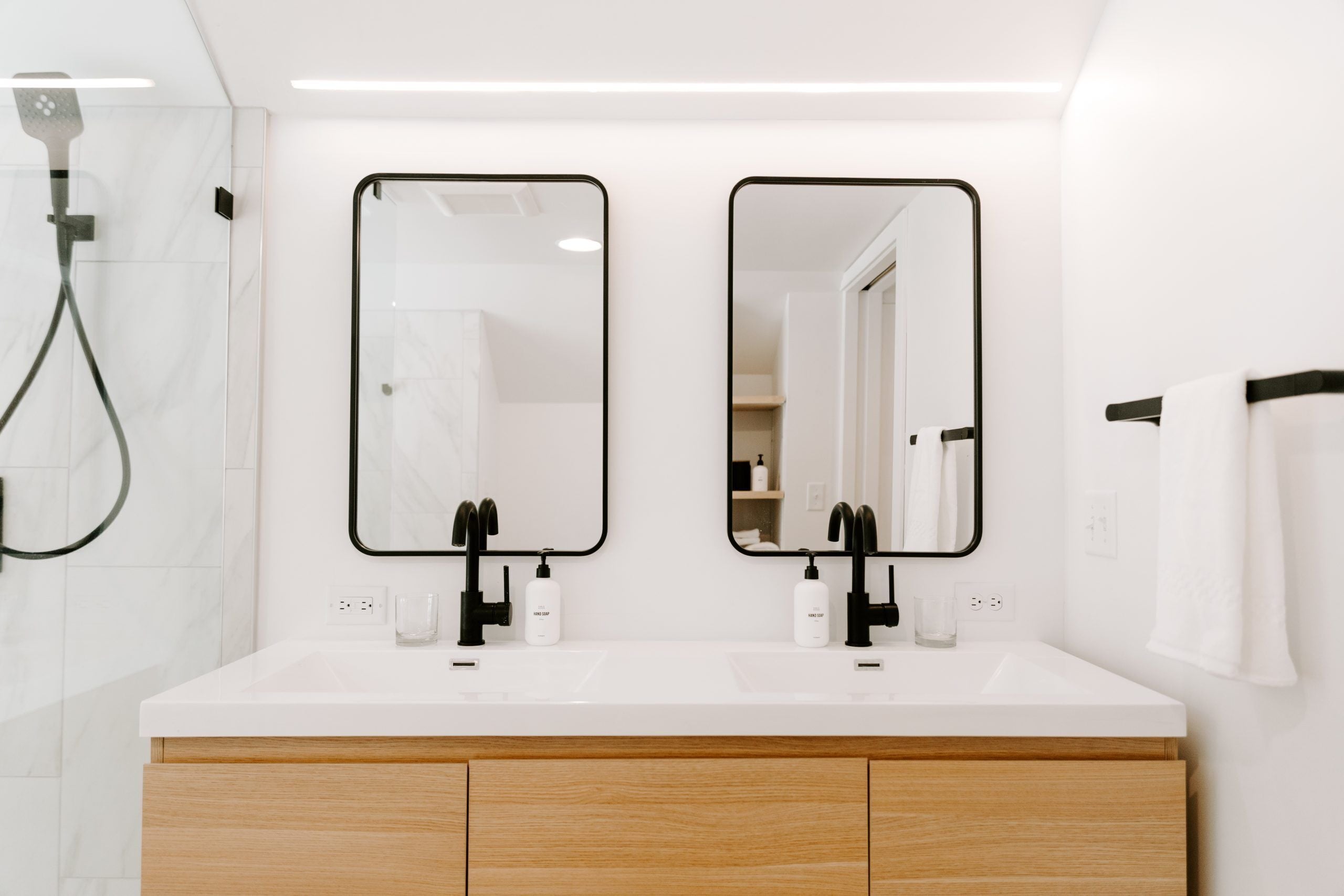 A modern bathroom with two sinks, black faucets, and a glass shower enclosure.
