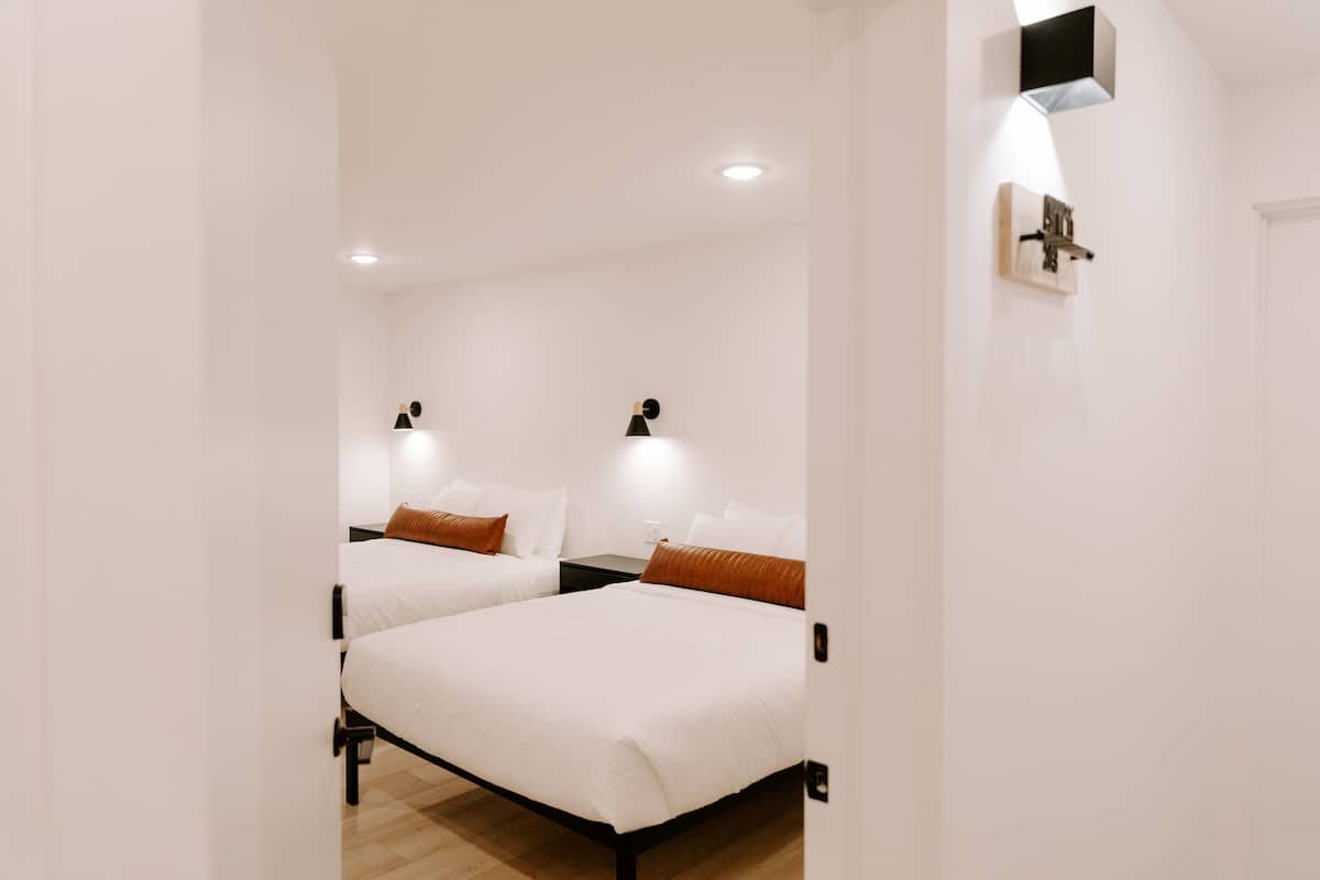A hotel room with two beds, a nightstand, a wall-mounted light, and a ceiling light.