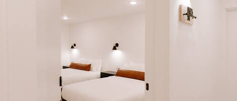 A hotel room with two beds, a nightstand, a wall-mounted light, and a ceiling light.