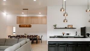 A modern kitchen with a central island, black bar stools, a dining area with a wooden table and chairs, and a grey sofa in a living area. - Nature Link Resort (Nisswa)