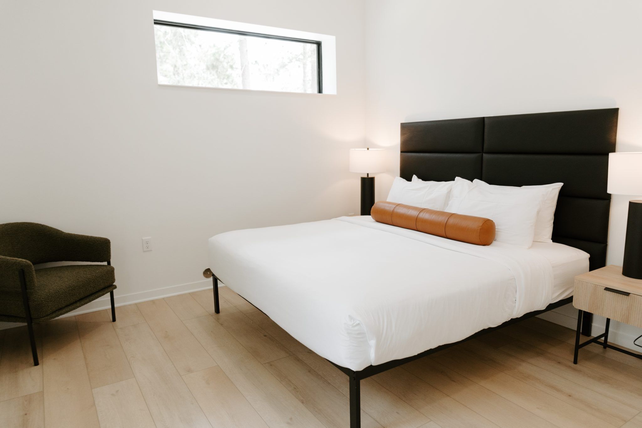 A modern bedroom with a large bed, two bedside lamps, a window, and a chair.