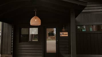 A dark wooden building entrance with a woven hanging light fixture, a door, and a window.