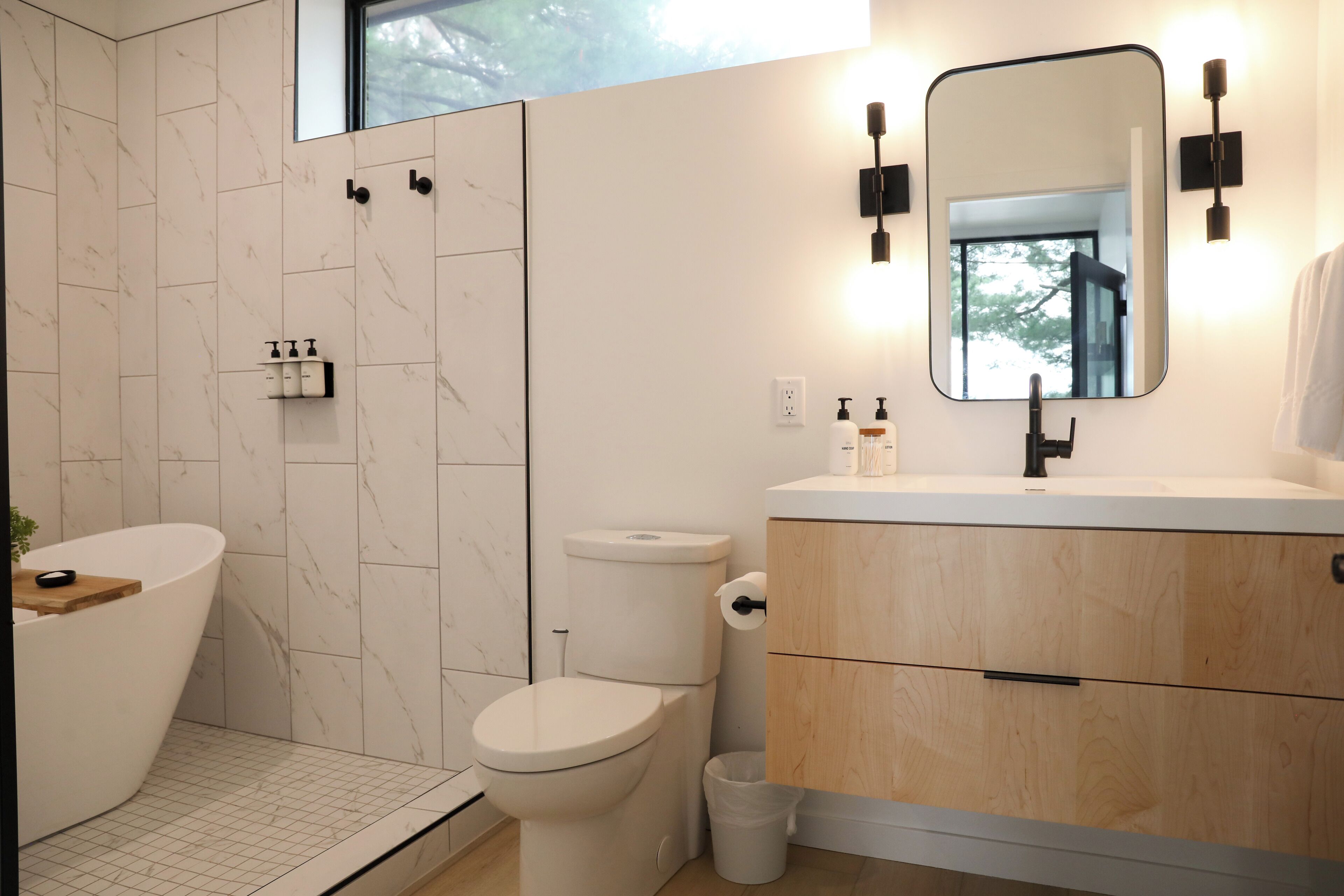 A modern bathroom with a freestanding bathtub, a toilet, and a vanity with a mirror.
