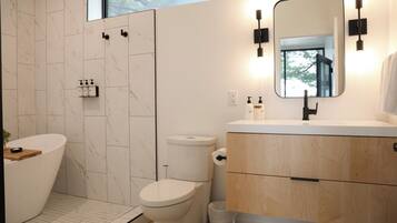 A modern bathroom with a freestanding bathtub, a toilet, and a vanity with a mirror.