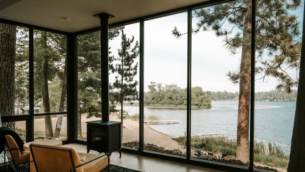 A modern room with large windows overlooking a lake, a cozy seating area, and a fireplace. - Nature Link Resort (Nisswa)