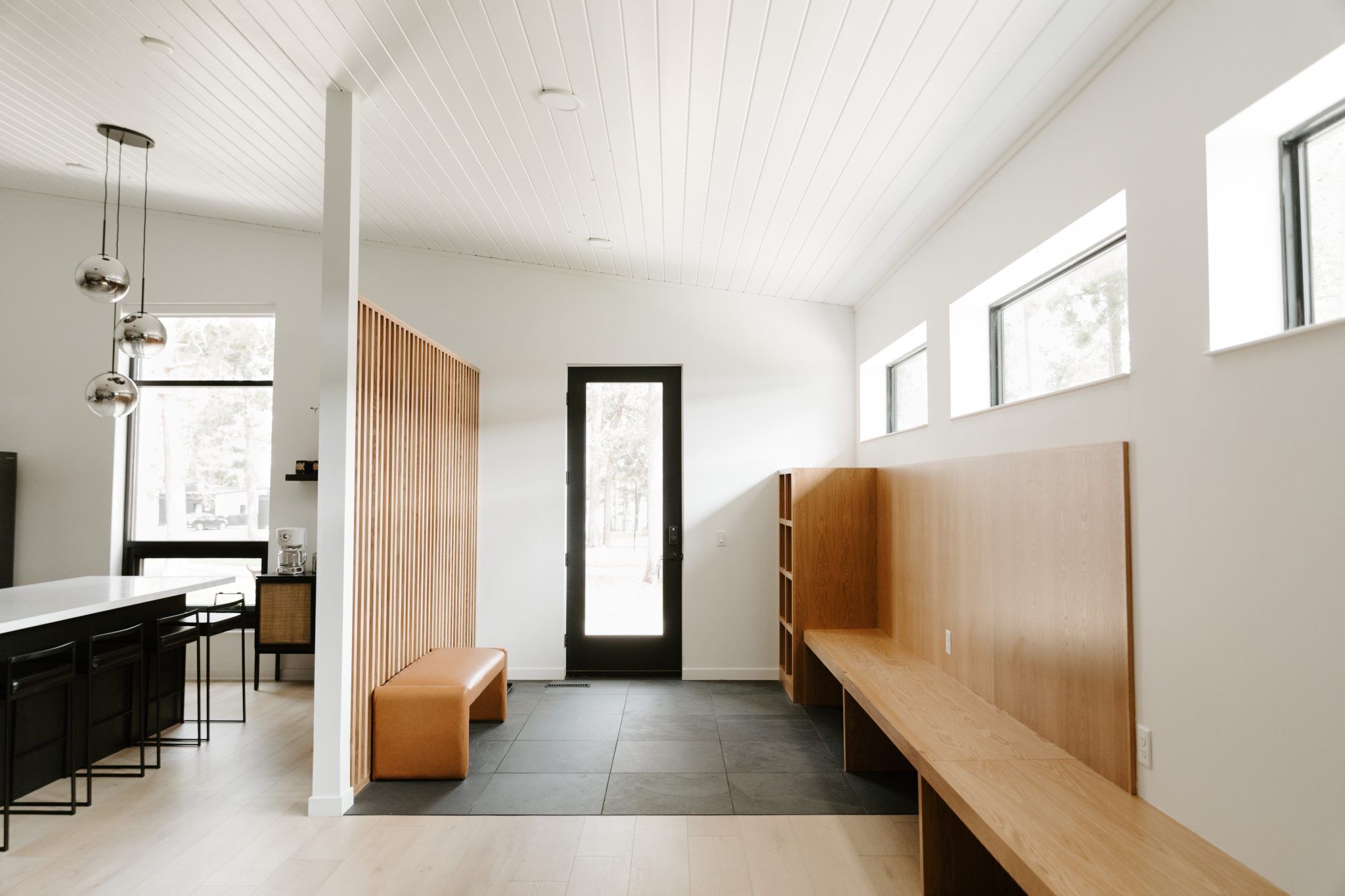 A modern interior with a long bench, a wooden partition, and a kitchen area with a counter and stools.