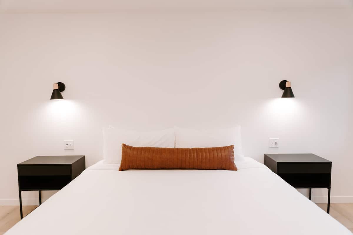 A minimalist bedroom with a large bed, two nightstands, and wall-mounted lamps.
