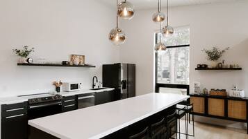 A modern kitchen with a large island, black cabinetry, white countertops, and pendant lighting.