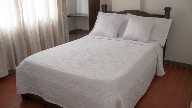 A neatly made bed with a white quilt, a wooden headboard, and a tiled floor. - Ayenda Maraná (Manizales)