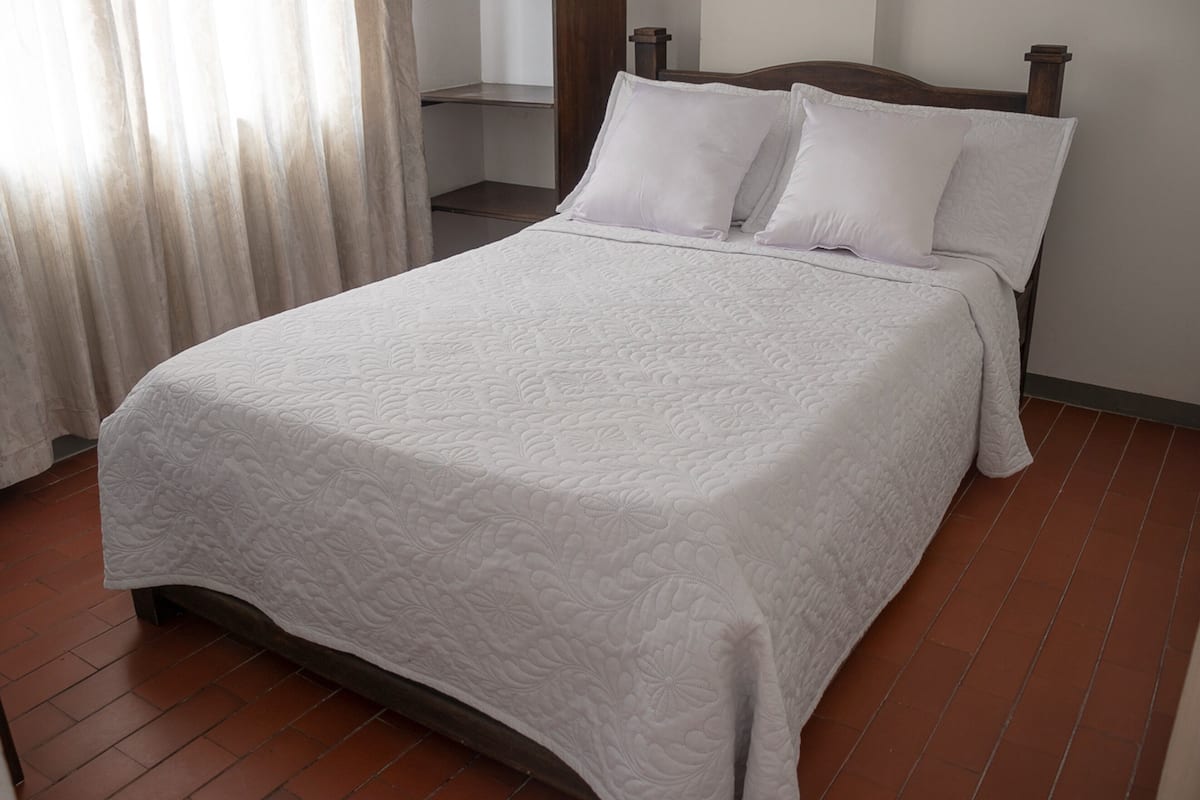 A neatly made bed with a white quilt, a wooden headboard, and a tiled floor.