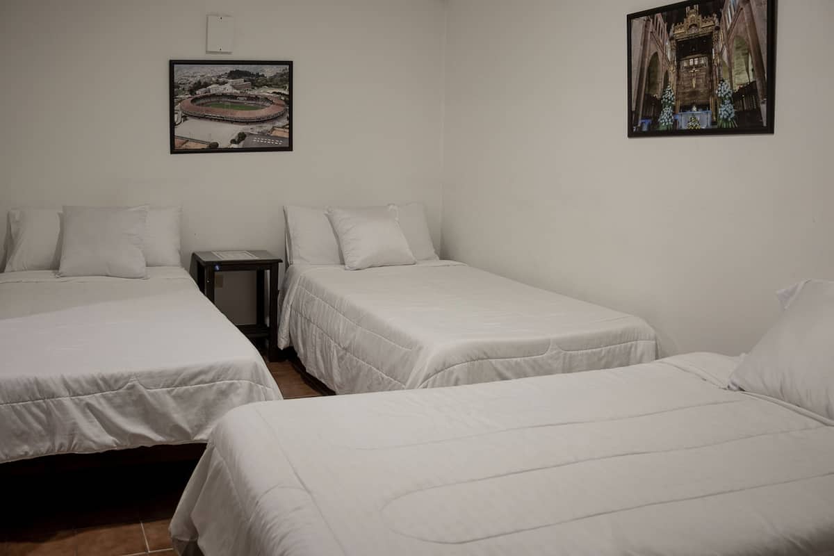 A hotel room with two single beds, a small table, and two framed pictures on the wall.