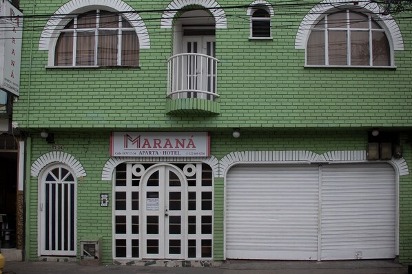Un edificio verde con un letrero que dice "MARANA APTA - HOTEL" y un gran portón de garaje.