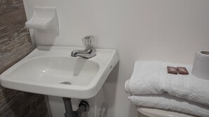 A bathroom with a white sink, a glass-faucet, a soap dish, and a toilet with a roll of toilet paper and a folded towel. - Ayenda Maraná (Manizales)