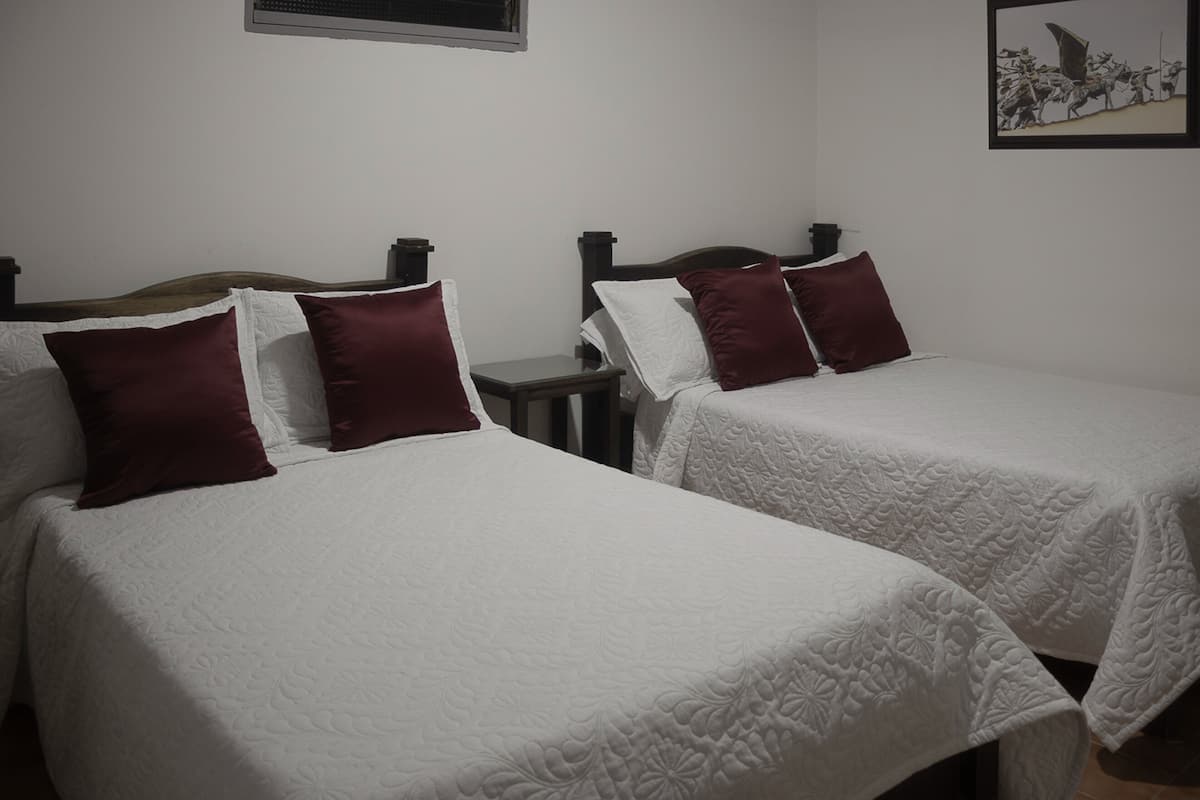 Two single beds with white bedding and maroon pillows, a small bedside table, and a framed picture on the wall.