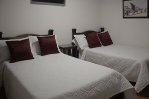 Dos camas individuales con ropa de cama blanca y almohadas color borgoña, una mesita de noche pequeña y un cuadro en la pared.