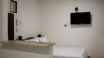 Una habitación sencilla con una cama, un escritorio de madera, un teléfono y un televisor montado en la pared.