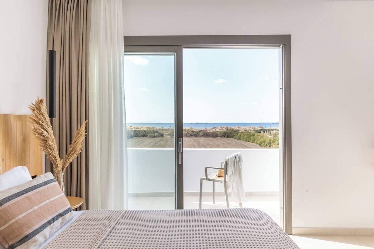 A bedroom with a bed, a chair, a view of the outdoors, and a window with curtains.
