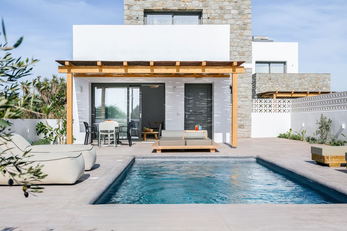 A modern outdoor pool area with a pergola, seating, and a stone building in the background.