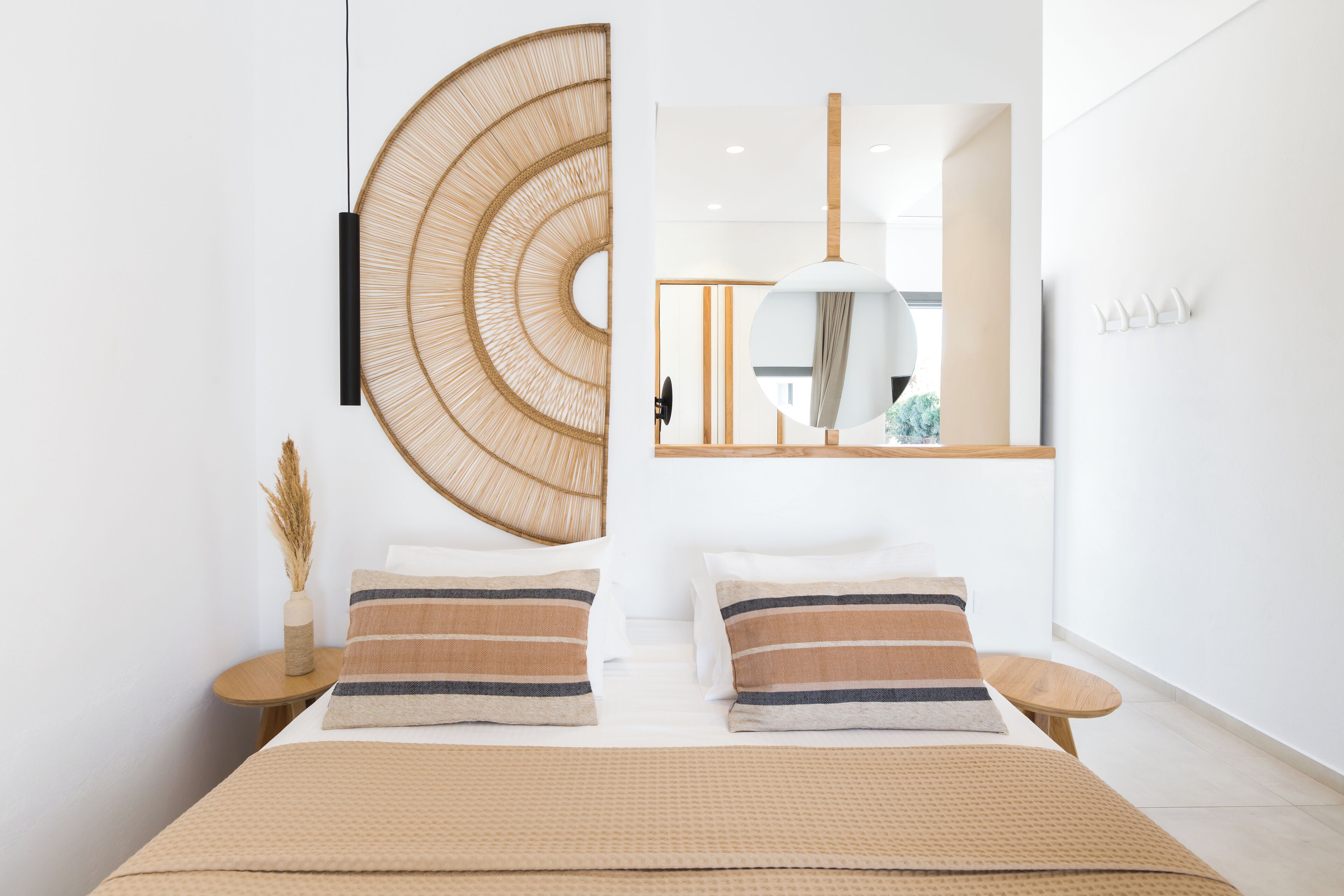A modern hotel room with a large bed, a round wall hanging, a mirror, and a small round table with a vase.