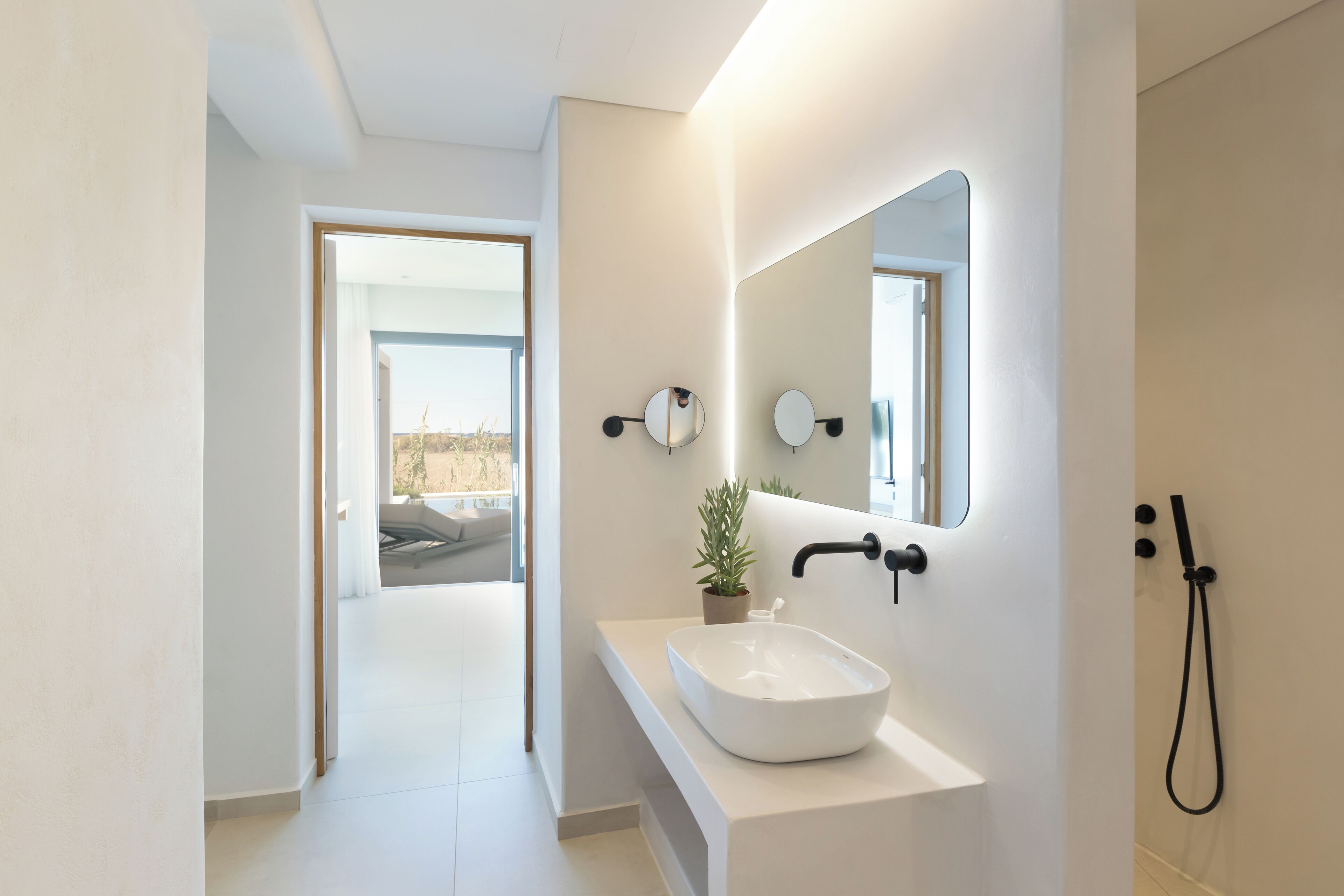 Une salle de bain moderne avec un lavabo blanc, deux miroirs ronds, une plante en pot et une douche.