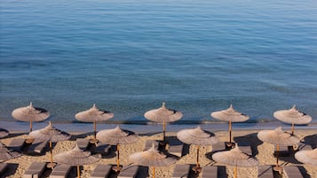 Una playa con filas de sillas de playa y sombrillas de paja.