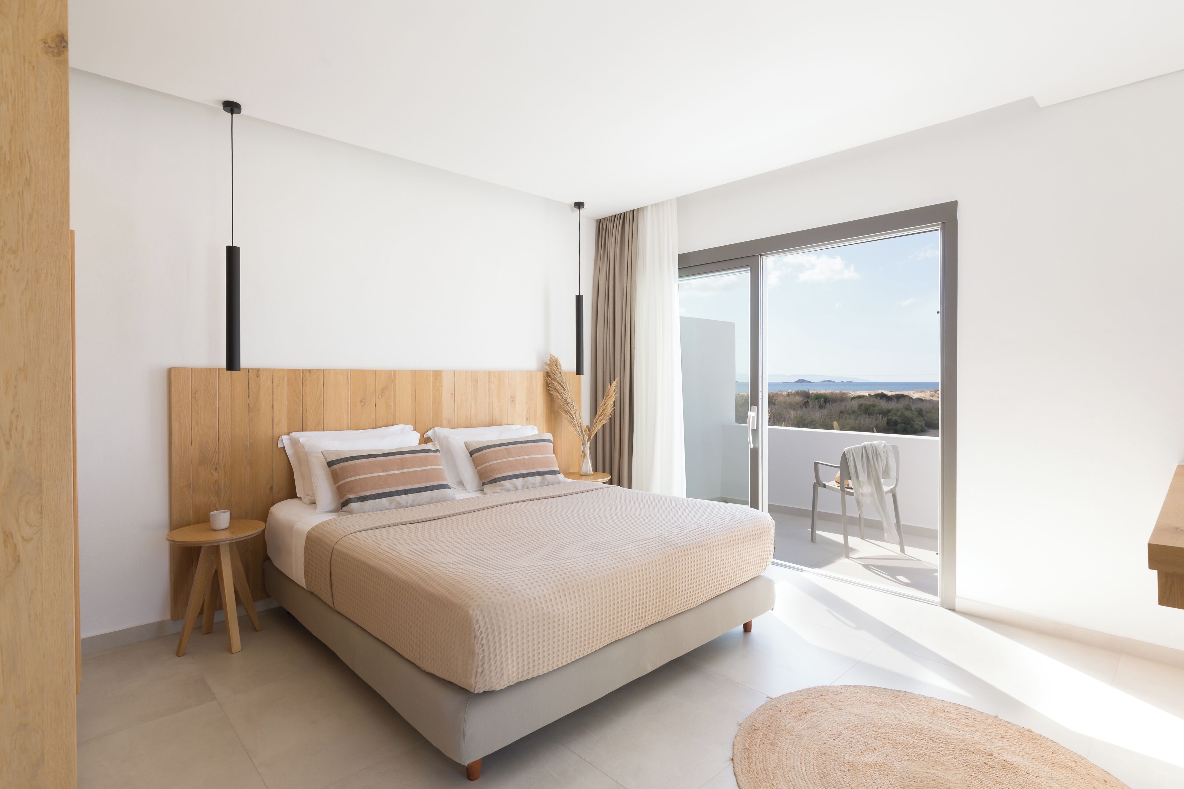 A modern bedroom with a large bed, a small side table, and a view of the outdoors.