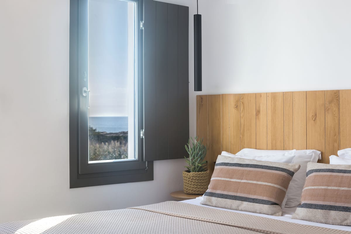 A bedroom with a bed, pillows, a potted plant, and a view through a window.