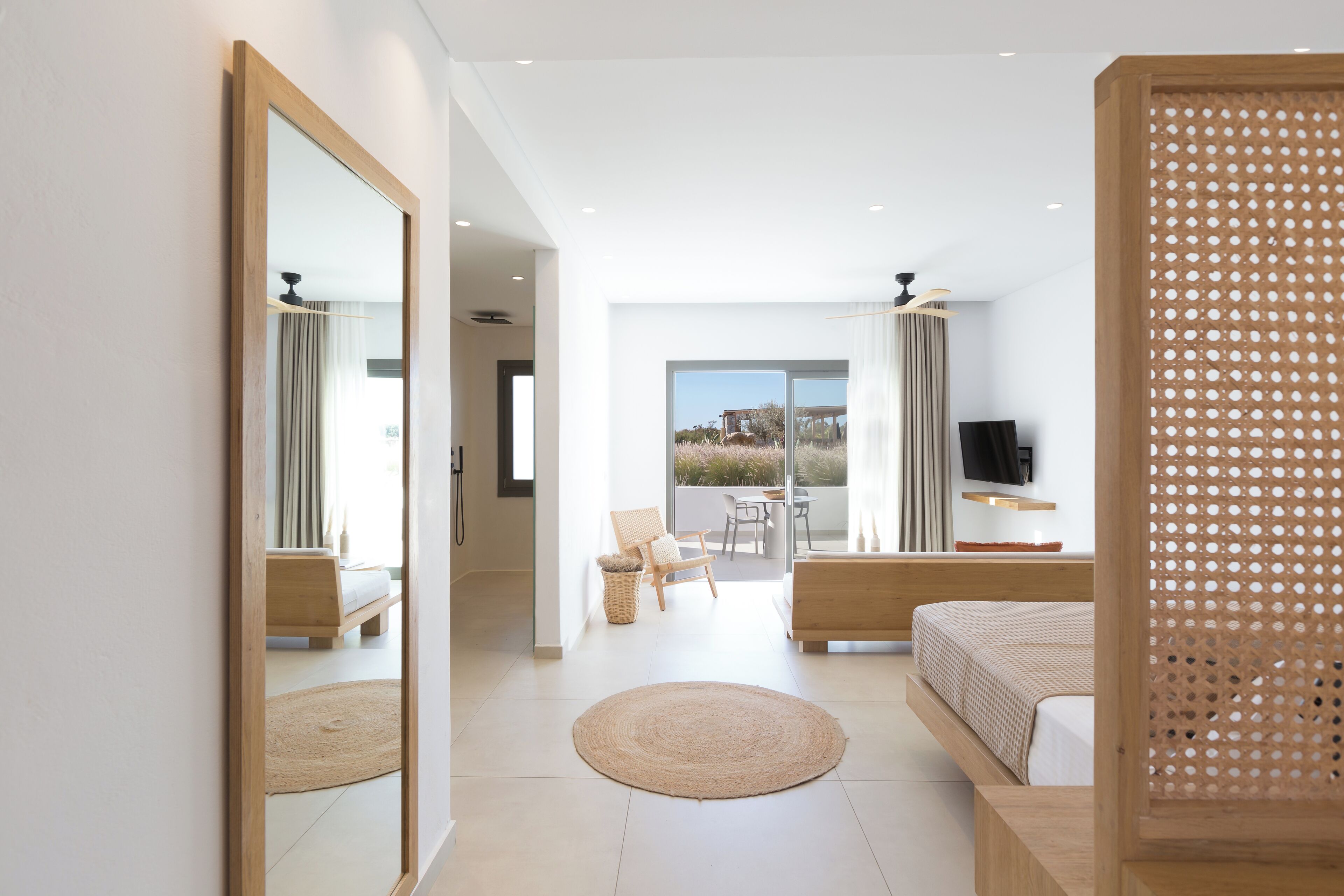 A modern bedroom with a large bed, a sitting area with a chair and table, a TV, and a balcony with a view.