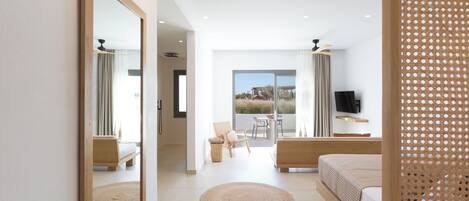 A modern bedroom with a large bed, a sitting area with a chair and table, a TV, and a balcony with a view.