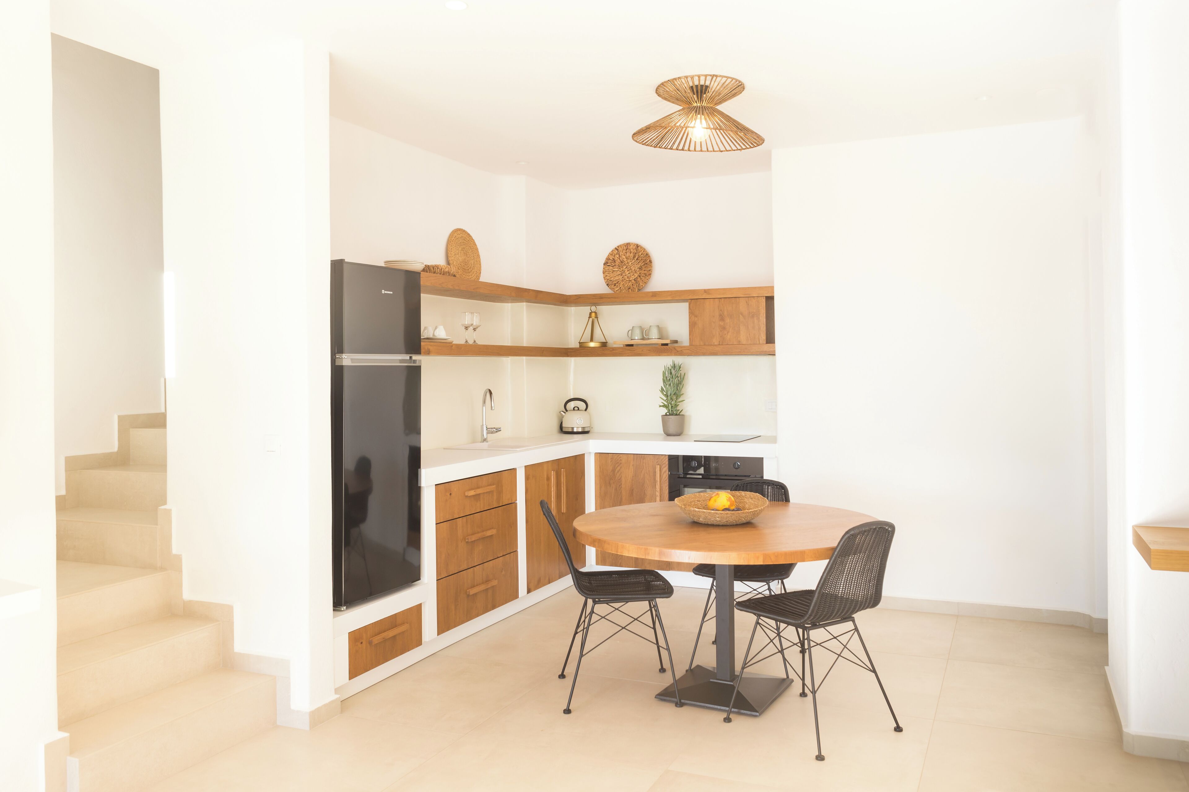 Une cuisine moderne avec des meubles blancs, un réfrigérateur noir et une table ronde en bois, accompagnée de chaises.