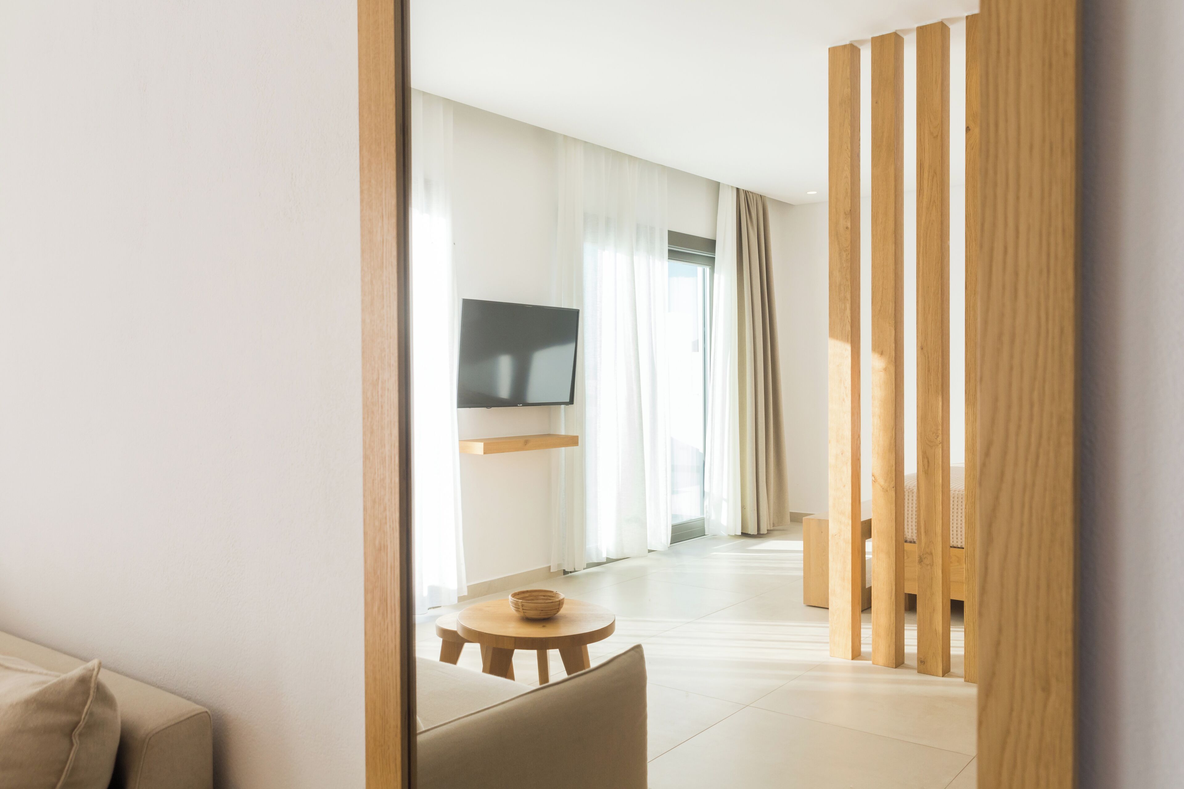 Moderni hotellihuone, jossa on pelkistetty sisustus. Huoneessa on sohva, pieni pyöreä pöytä ja seinälle asennettu televisio.
