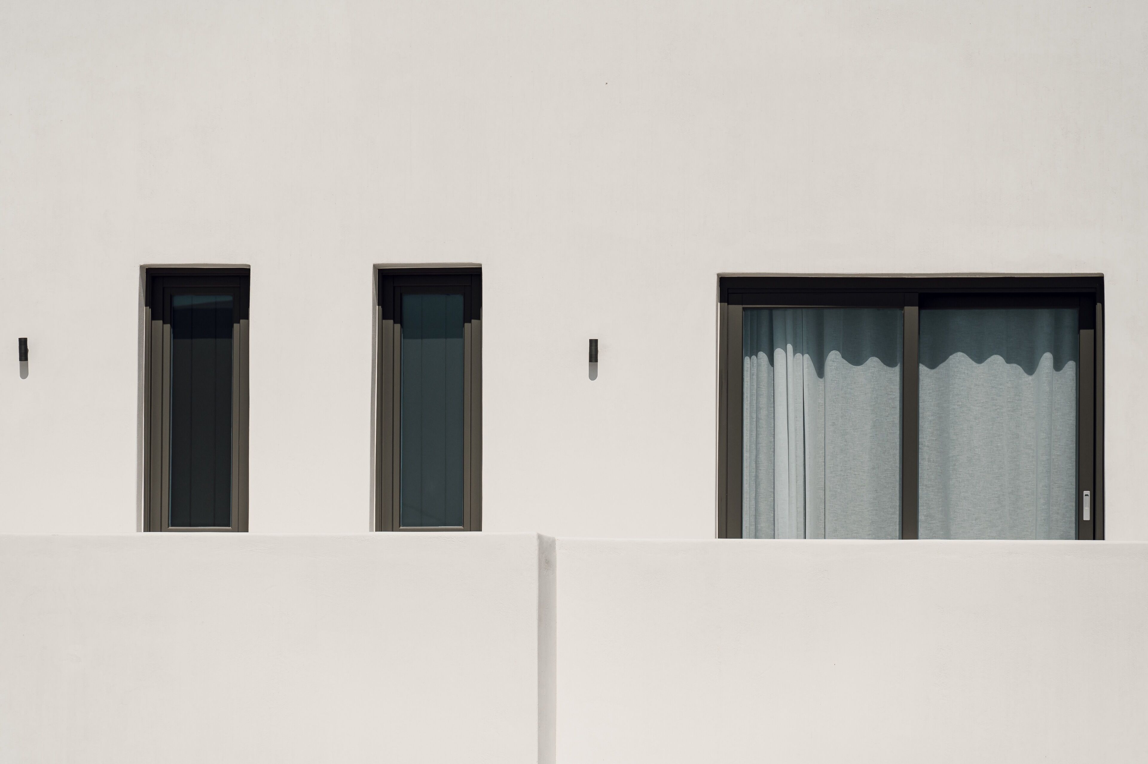 A building facade with three windows, two of which have dark frames and one with a curtain.
