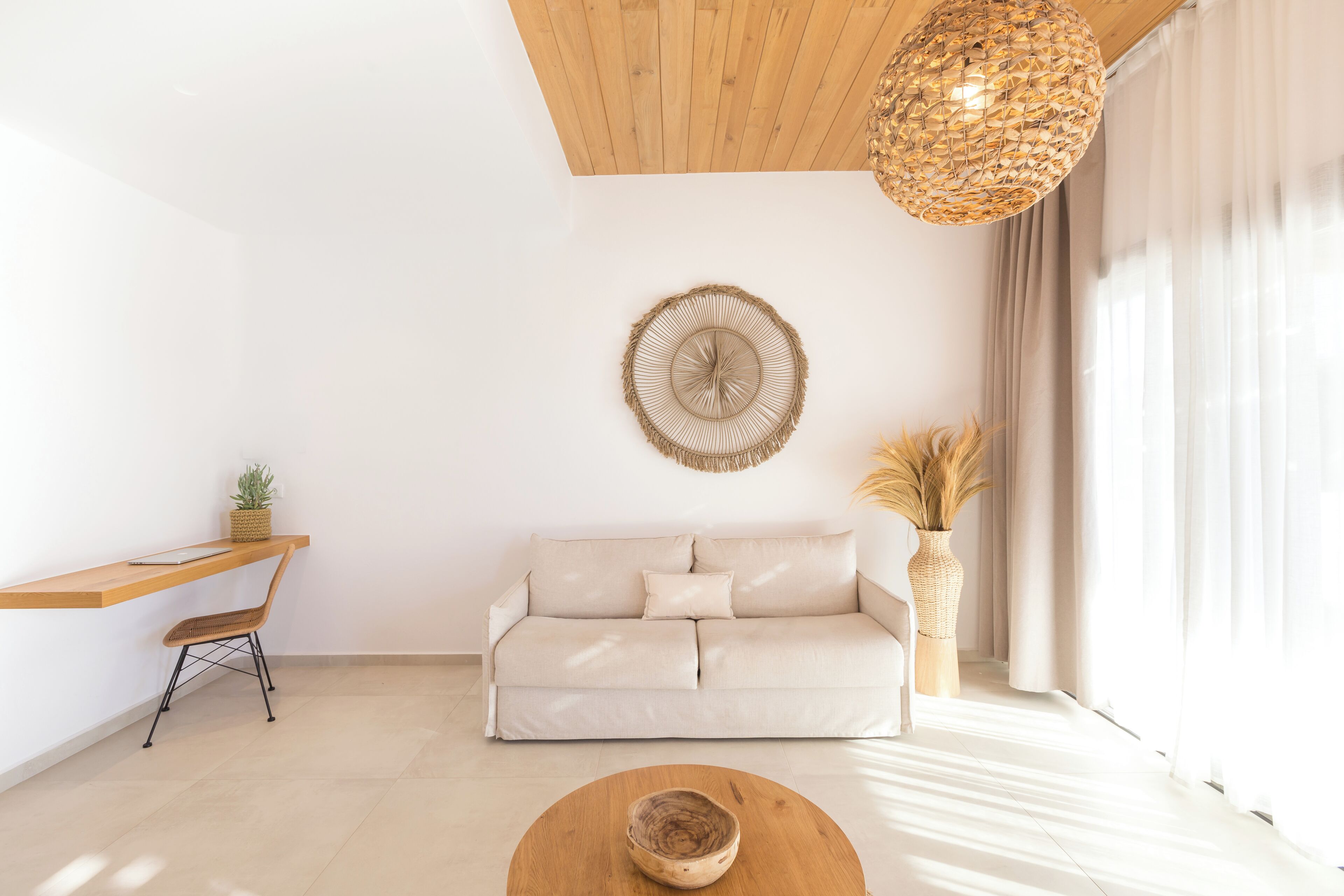 Un salon minimaliste avec un plafond en bois, un canapé blanc, une table basse en bois et un luminaire en fibres tressées.