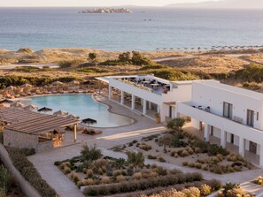 A modern resort with a swimming pool, outdoor seating, and a view of the sea. - Sundunes Hotel Naxos  (Naxos)