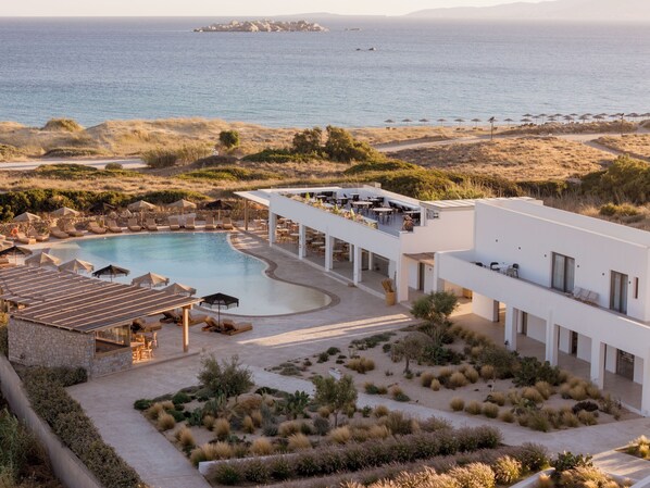 A modern resort with a swimming pool, outdoor seating, and a view of the sea. - Sundunes Hotel Naxos  (Naxos)