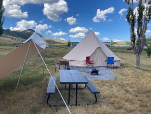 Two tents sit on a grassy field, accompanied by a picnic table and portable stove.