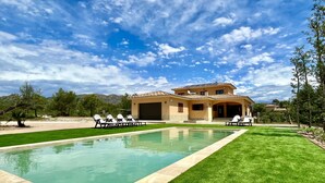 Une maison à deux étages avec une piscine, entourée d’une pelouse bien entretenue et d’arbres.