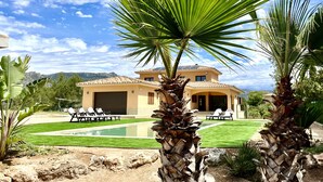 Une maison à deux étages avec une piscine, entourée de palmiers et d’une pelouse bien entretenue.