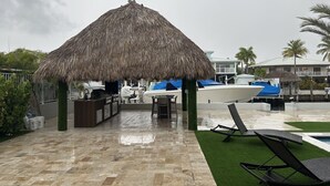 A covered outdoor area with a thatched roof, a pool, and lounge chairs. - Relaxing home in a beautiful location with luxurious accommodations (Key Largo)