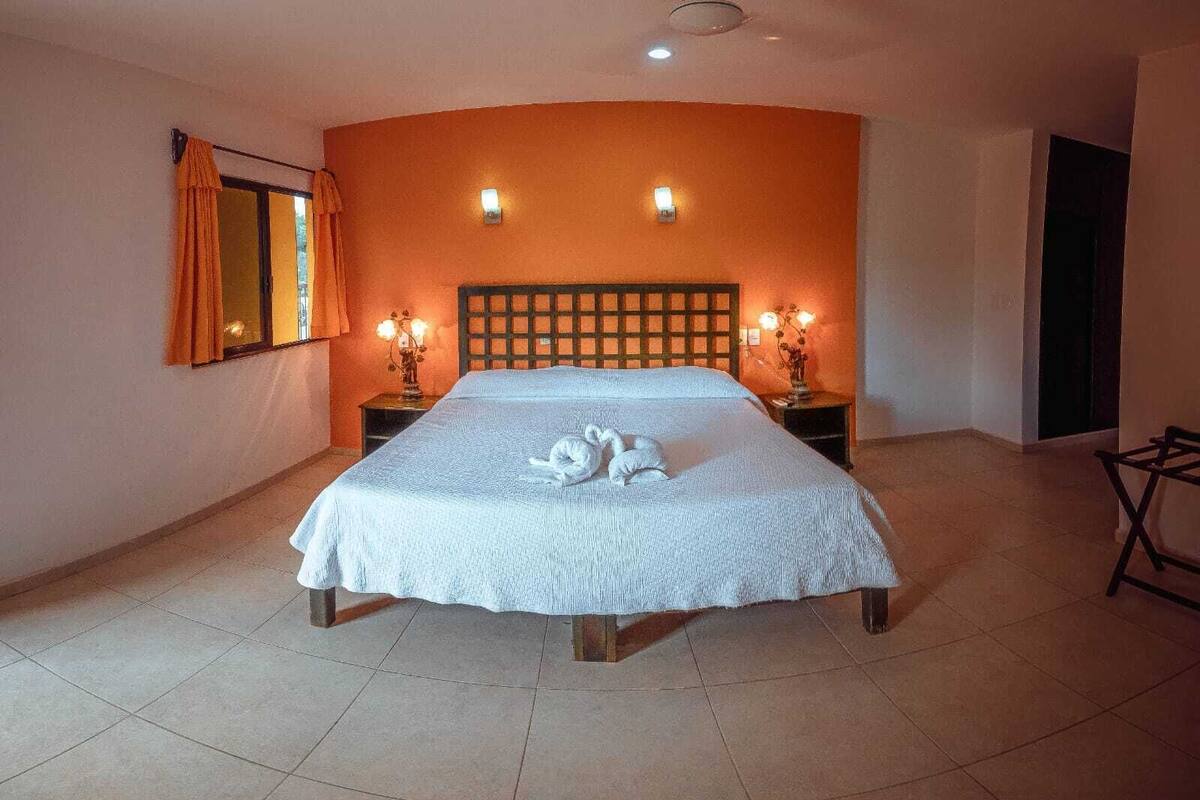 A hotel room with a bed, two bedside lamps, a window with curtains, and a wall-mounted light fixture.