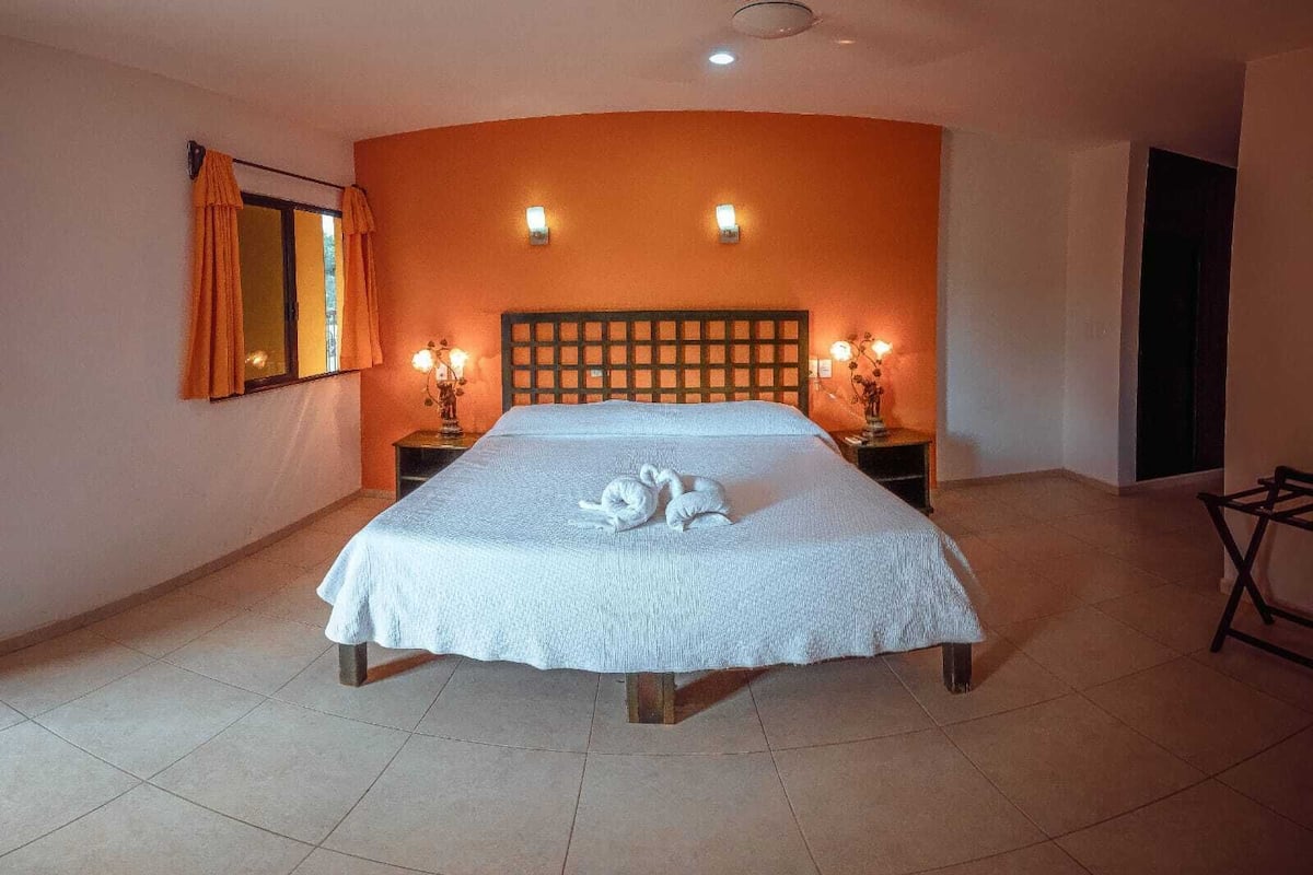 Habitación de hotel con cama, dos lámparas de noche, ventana con cortinas y un aplique en la pared.