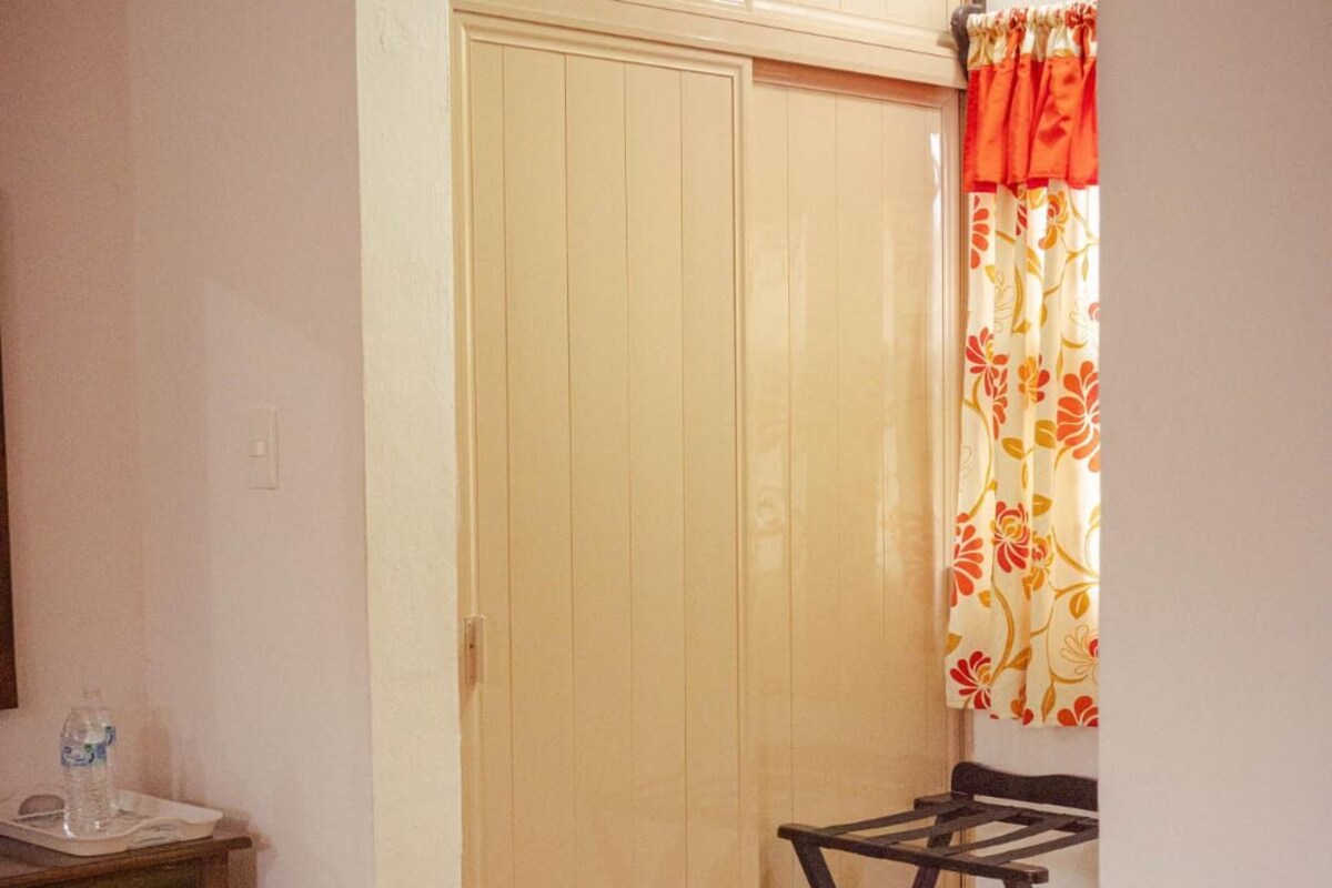 Una habitación con un armario de madera, una mesita con una botella de agua y una silla.